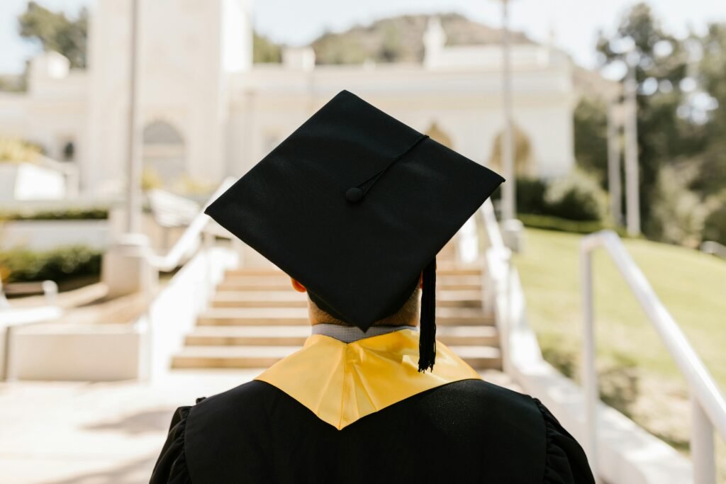 pexels-photo-7713511-7713511 Back view of a graduate in a cap and gown standing outdoors facing a building.