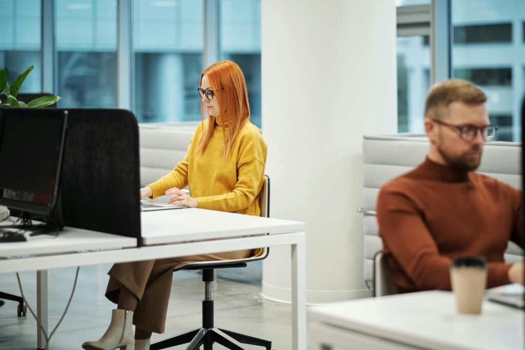 Two professionals working in a contemporary office environment with computers and casual attire.